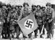 American paratrooper, among the first to make successful landings on the continent, holds a Nazi flag captured in a village assault. Utah Beach, St. Marcouf, France. 8 June 1944
